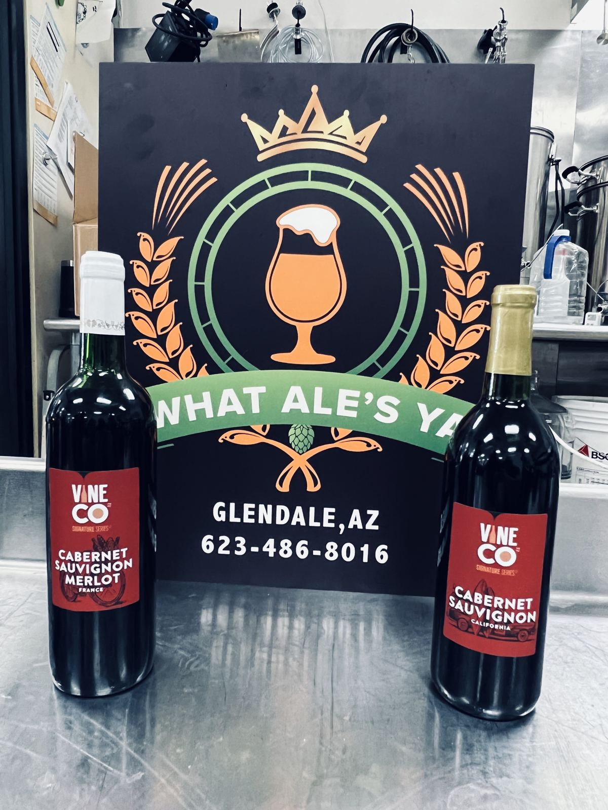Bottles of house-made wine in front of the What Ale's Ya logo